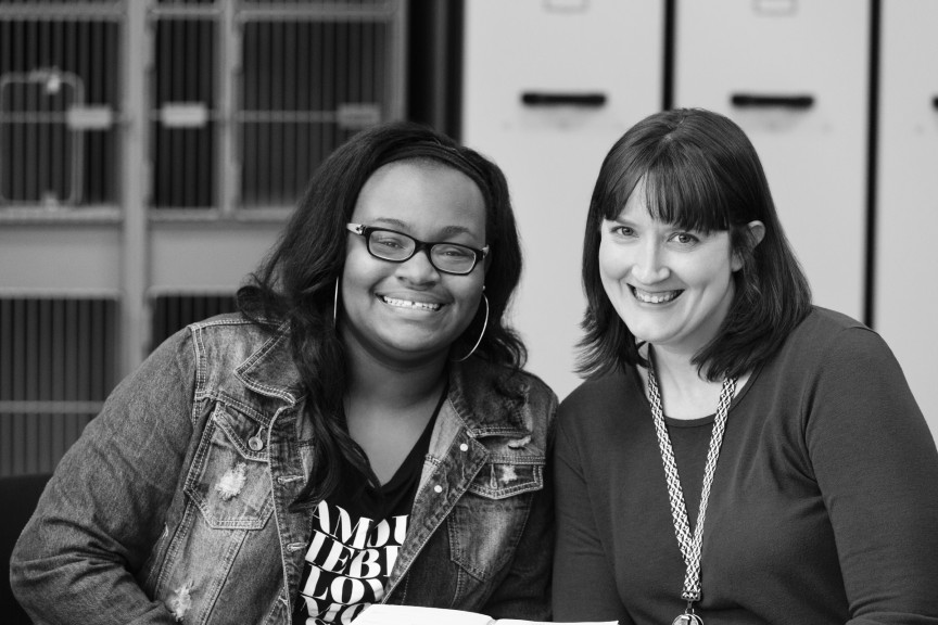 Student Symone sits next to marketing employee Katie. Both are leaning in and smiling.
