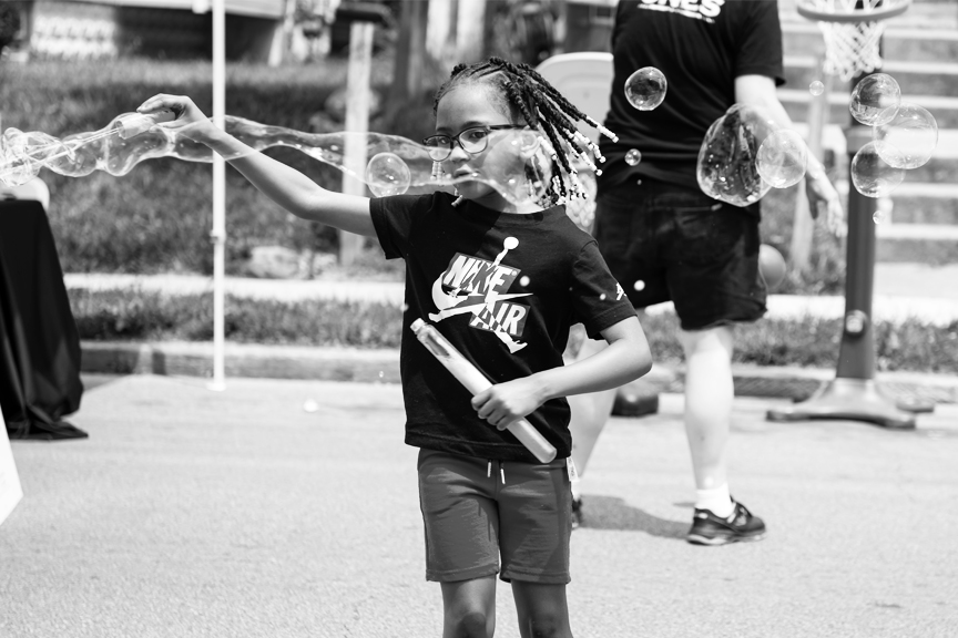 An elementary aged child is happily making huge bubbles while playing in the neighborhood.