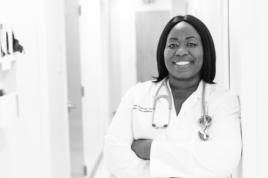 Dr. Amponsah is smiling and wearing a white coat in a primary care office.