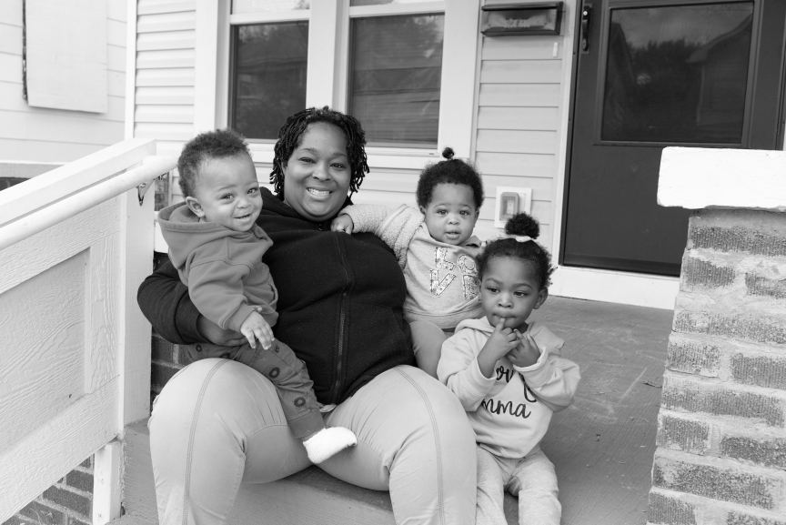 A mom is sitting on front porch steps, smiling with her three young kids