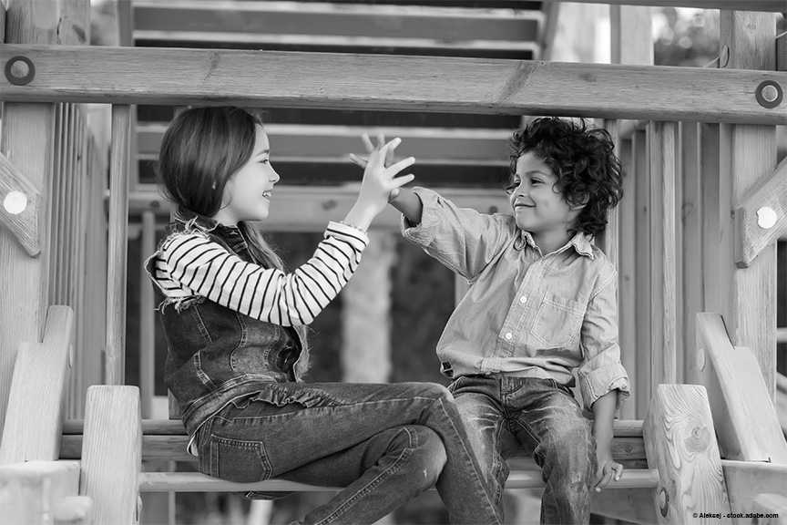Two young children are playing on a wooden playset, giving each other a "high-five".