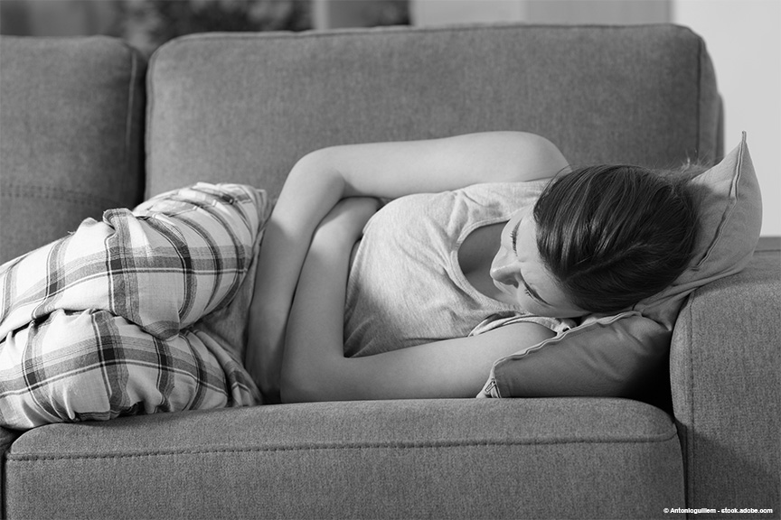 A teen girl is wearing plaid pajamas, laying on the couch. Her arms are wrapped around her stomach.