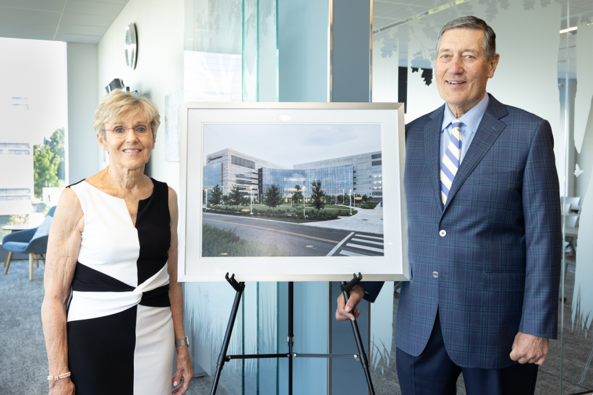Two donors are smiling, standing next to an easel that is holding a large photo of a building exterior.