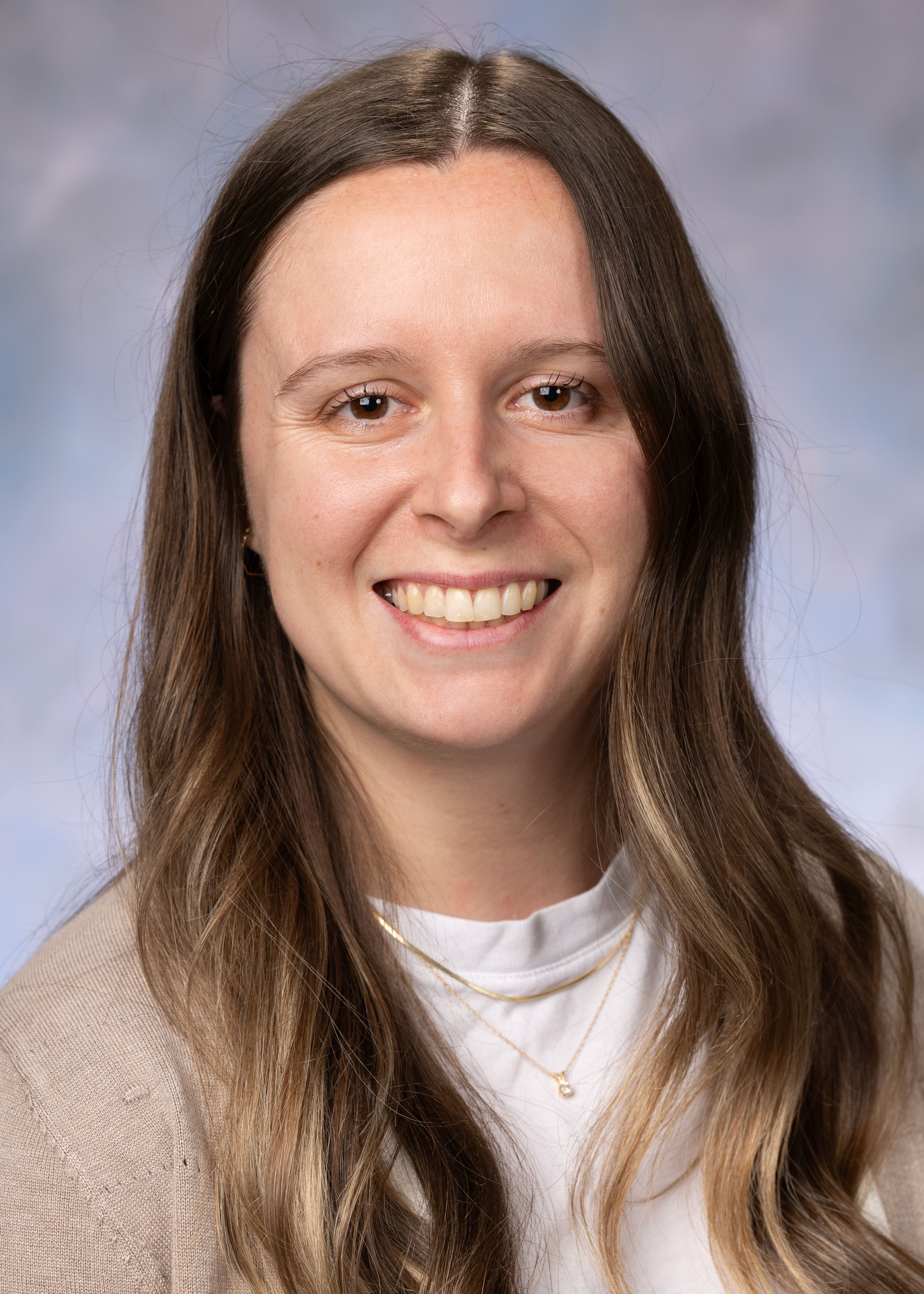Portrait of Lauren Walsh, MPH. She las long brown hair and is wearing a white shirt with a brown cardigan.