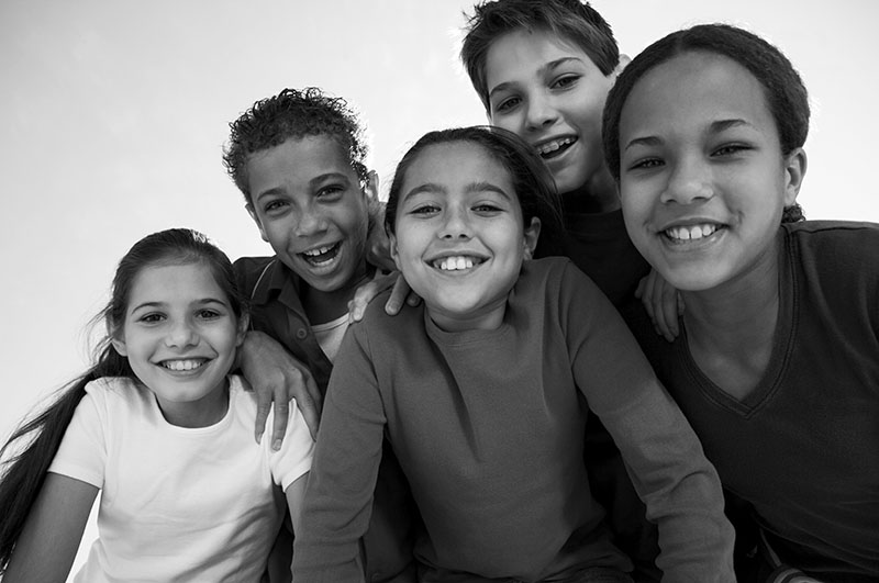 A group of five older elementary aged kids lean forward toward the camera, all smiling.